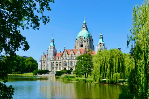 pexels-photo-17360696-17360696 Scenic view of the New Town Hall in Hanover with lush greenery and lake reflection.